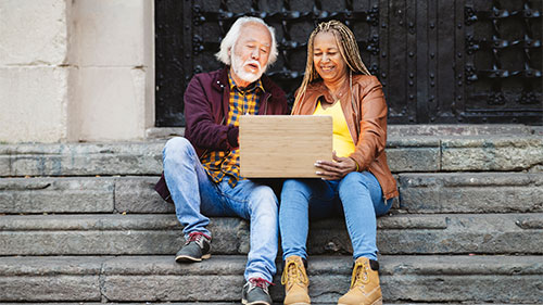 two older people sitting on stoop looking at laptop