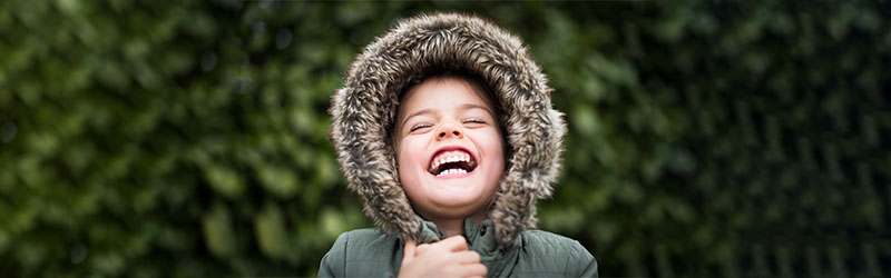 young girl with eyes closed in winter coat smiling with mouth open