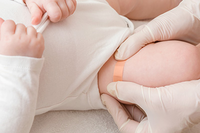 Gloved hands placing bandage on an infant's thigh