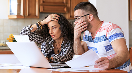 couple sitting at kitchen table reviewing bills and looking stressed