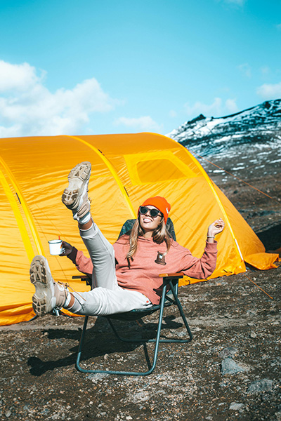 woman in camping chair by camping tent on side of snowy mountain